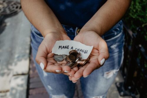 両手にコインと「Make A Change」と書いたメモを乗せている女性