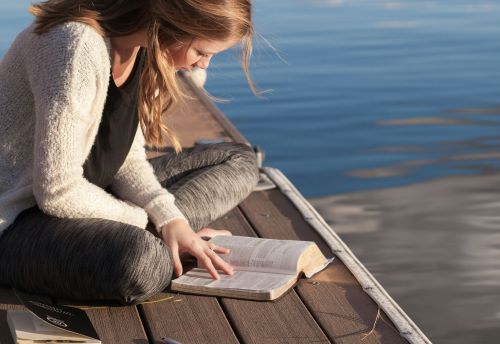 海辺で本を読む女性。リモラボで学ぶ女性のイメージ。